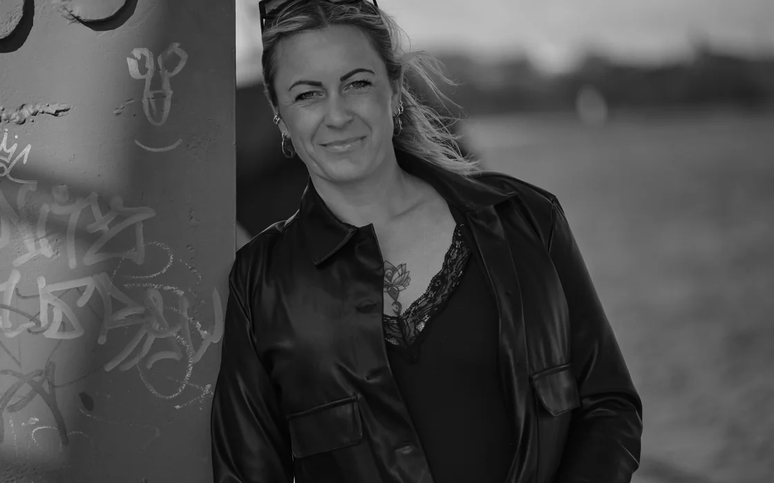 Schwarzweisses Portrait einer Frau, die an einem Stahltraeger am Strand lehnt.